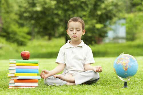 boy practicing meditation with school books beside him