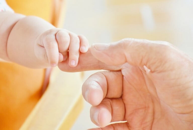 Bebé cogiendo un dedo de su padre por reflejos de prensión