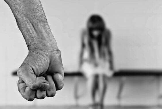 Brazo de un hombre y mujer sentada con miedo por la violencia