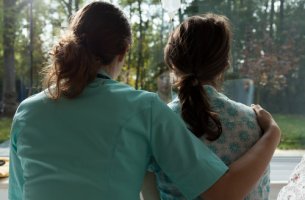 Enfermera abrazando a una mujer con cáncer de mamá mientras miran por la ventana