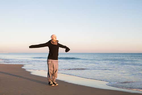 Mujer con cáncer en la playa con los brazos abiertos