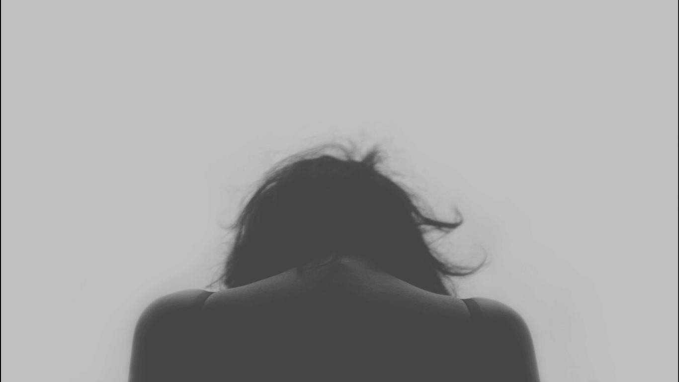 Mujer de espaldas con la cabeza hacia abajo con dolor crónico