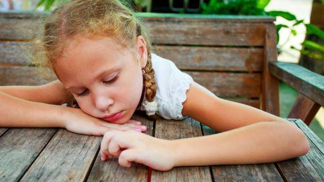Niña con depresión apoyada sobre una mesa
