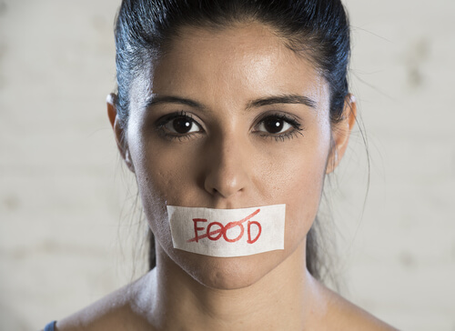 Mujer con un cartel en la boca en el que la palabra comida está tachada