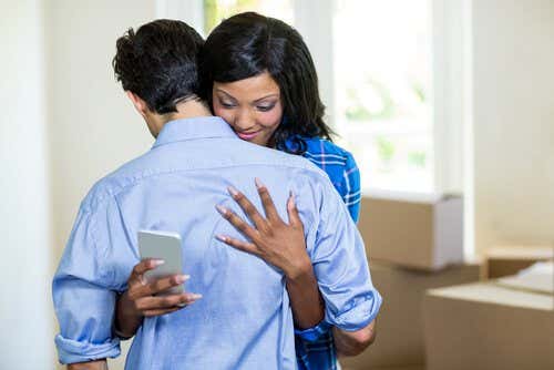 Mujer infiel abrazando a su marido mientras ve el móvil