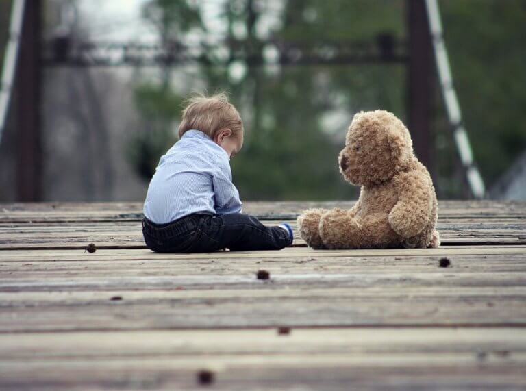 Niño sentando con un oso de peluche