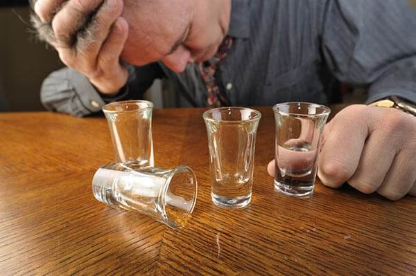 Hombre alcohólico con copas vacías en la mesa