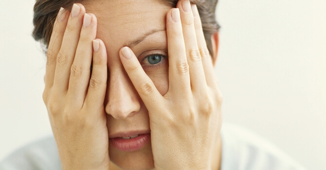 A woman covering her face and one eye.