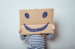 Niño con un cartón que tiene una cara sonriente dibujada