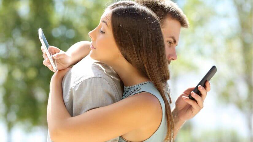 Pareja mirando el móvil mientras se abraza