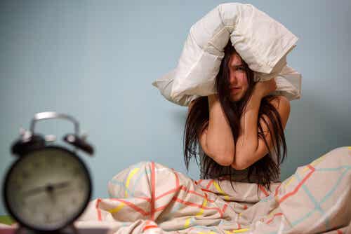 Chica adolescente con almohada en la cabeza mientras suena el despertador