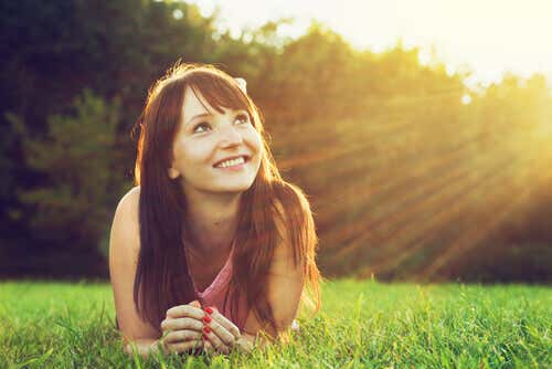 Chica sonriendo mirando al sol y pensando de forma optimista