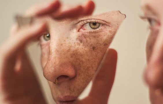 chico sujetando cristal donde se refleja su rostro como resultado de los sesgos cognitivos