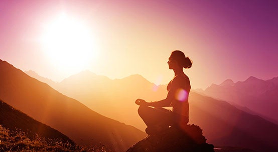 Mujer meditando en una montaña al amanecer intentando conectar con su abundancia
