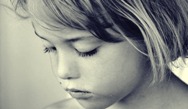 Niña triste con los ojos cerrados al sufrir el robo de la infancia