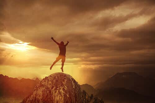 Hombre saltando en la cima de una montaña feliz por aplicar las técnicas de control emocional