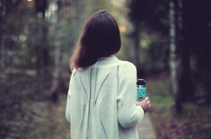 Mujer con vaso en la mano ante un camino preguntándose ¿Debo irme o debo quedarme?