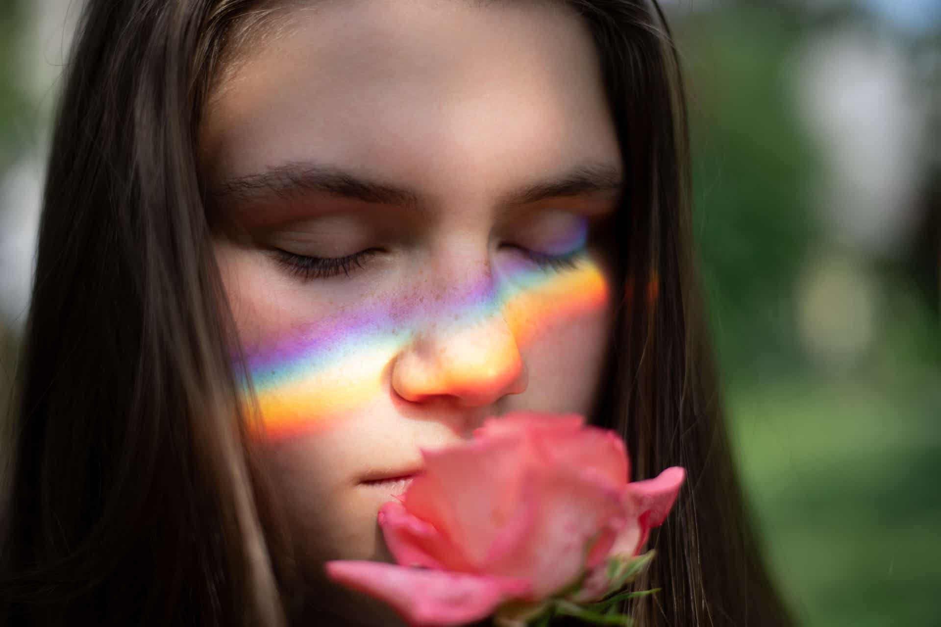 Mujer oliendo una rosa con el reflejo del arco iris en sus mejillas y pensando en los recuerdos del ayer