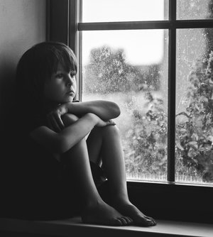 Niño triste sentado en una ventana