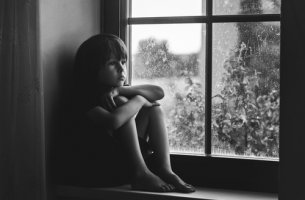 Niño triste sentado en una ventana para representar a los niños con baja autoestima