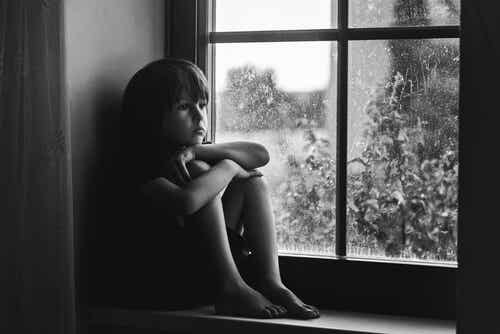 Niño triste sentado en una ventana para representar a los niños con baja autoestima