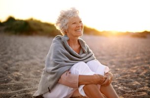 mujer mayor sentada en la playa feliz por envejecer saludablemente