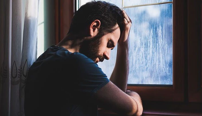 Sad man at a window suffers from reactive depression
