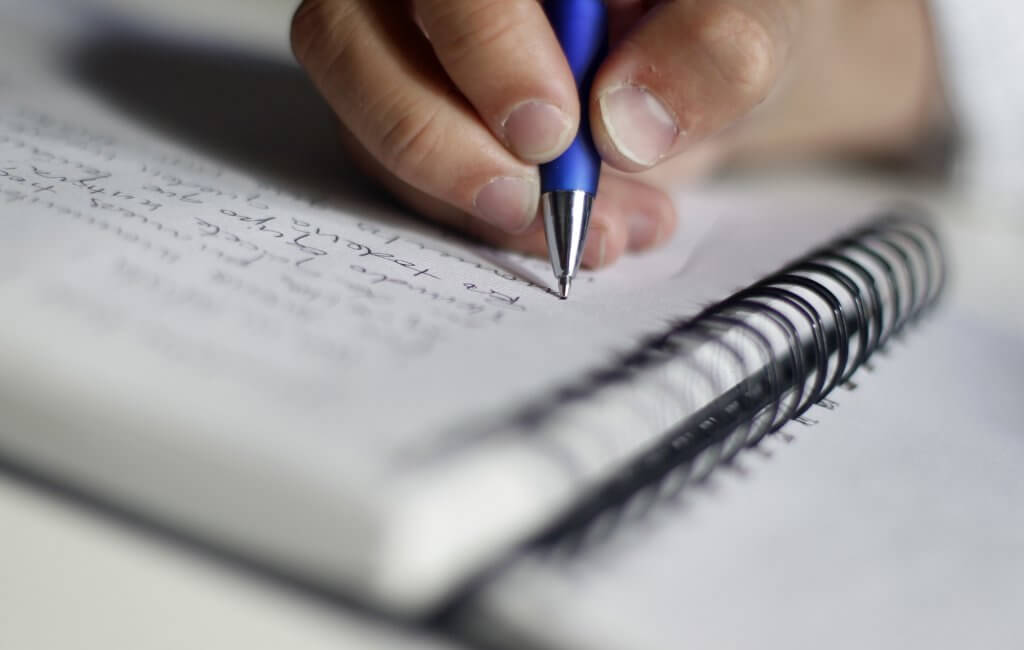 Mano escribiendo en una libreta aplicando la técnica Feynman