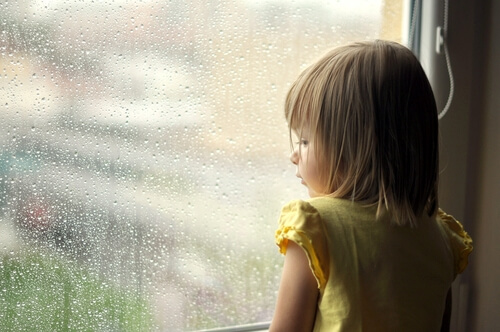 Niña mirando por la ventana que sufre heridas emocionales del pasado