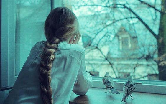 chica en la ventana con pájaros experimentando melancolía