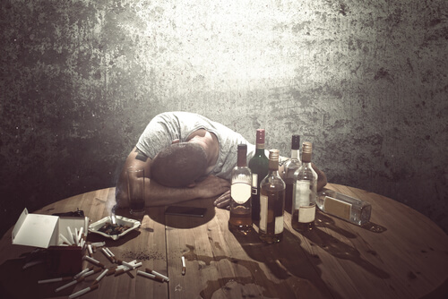 Hombre con la cabeza en la mesa y muchas botellas de alcohol