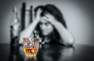 Mujer con una copa de alcohol y las manos en la cabeza para representar el trastorno por consumo de alcohol