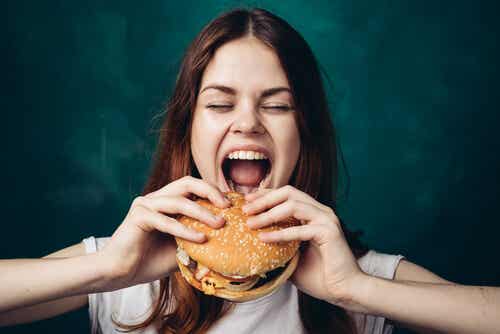 Mujer comiendo hamburguesa por hambre emocional