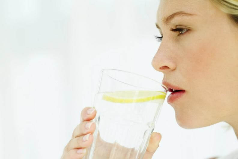 Mujer que bebe agua tibia con limón por las mañanas