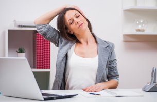 Mujer haciendo estiramientos de cuello en la oficina para representar los ejercicios de pausas activas
