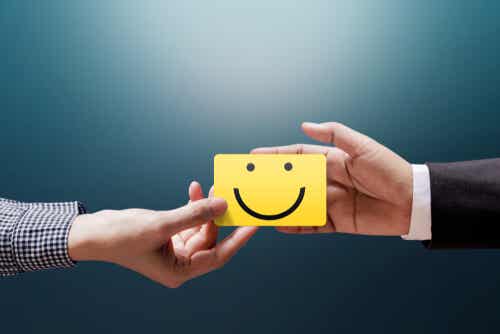 Empresario y cliente sujetando nota con una cara sonriente simbolizando cómo mejorar tu Inteligencia Emocional.