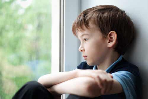 Niño triste mirando por la ventana que sufre los efectos de la intimidación 