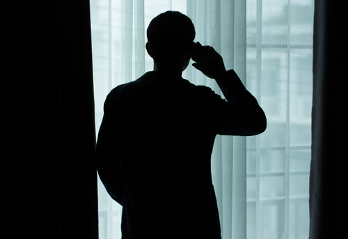 Hombre mirando por la ventana mientras habla por teléfono