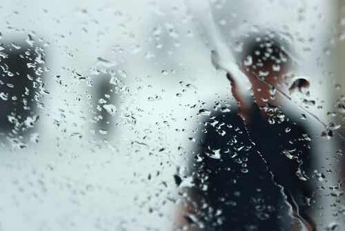 Silueta de un hombre tras un cristal con lluvia para representar opuesto a la depresión