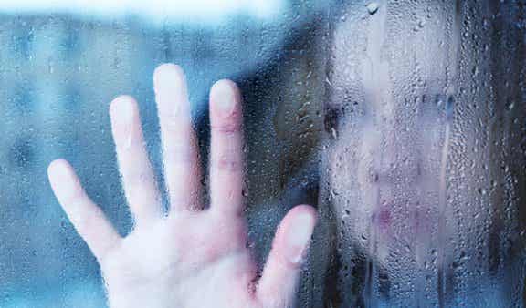 Mujer con una mano sobre una ventana con gotas de lluvia