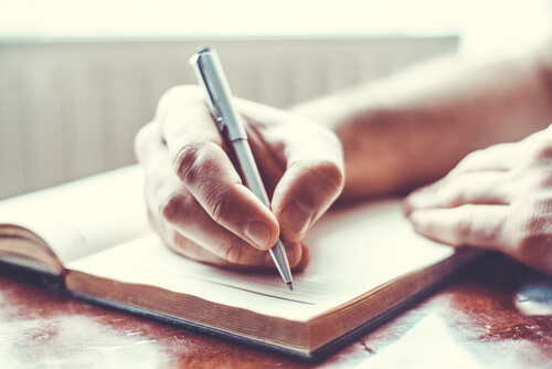 Mano escribiendo notas manuscritas en una hoja en blanco