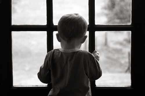Niño triste y solo mirando por la ventana sintiendo el peso de una herida abierta