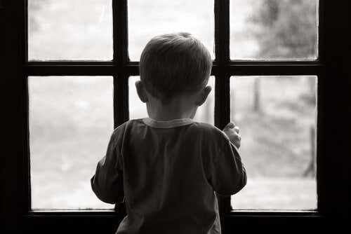 Niño triste y solo mirando por la ventana