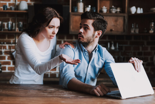 Chica mirando a su novio cuando está con el ordenador sospechando una infidelidad online