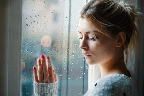 Kvinde ved vindue med regn på