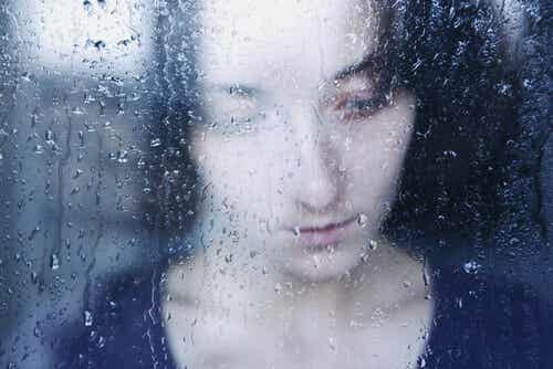 Mujer triste tras una ventana pensando en los vacíos emocionales