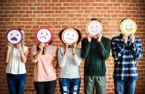 teenagers holding emoji faces representing different emotions in front of their faces.