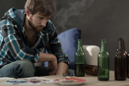 Chico joven con botellas de alcohol en la mesa