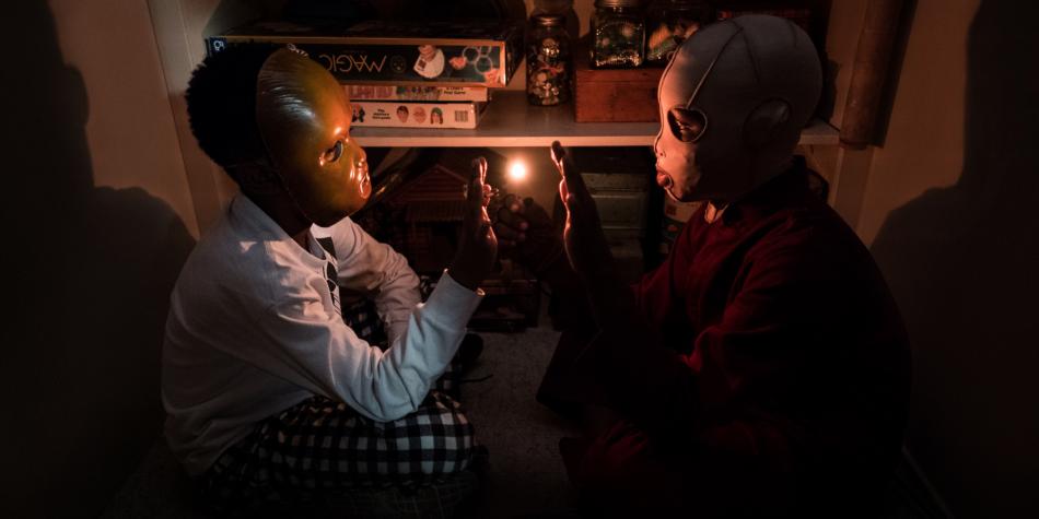 Niños con máscaras sentados enfrente uno del otro, escena de Nosotros