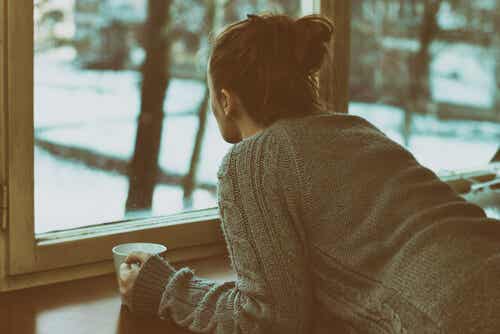 Femme buvant du café à une fenêtre en pensant à la solitude